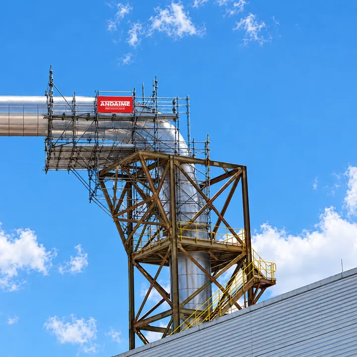 Andaime montado ao redor de uma tubulação industrial, com a placa da Andaime, sob céu azul